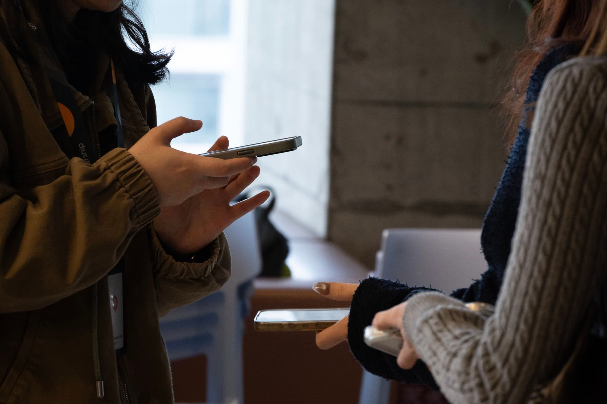 Two people standing indoors holding smartphones and a coffee mug