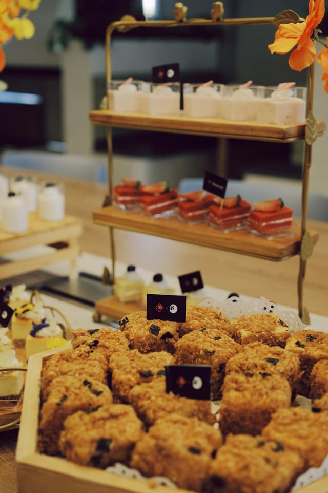 Assorted pastries and desserts arranged on a tiered wooden display stand with small label cards