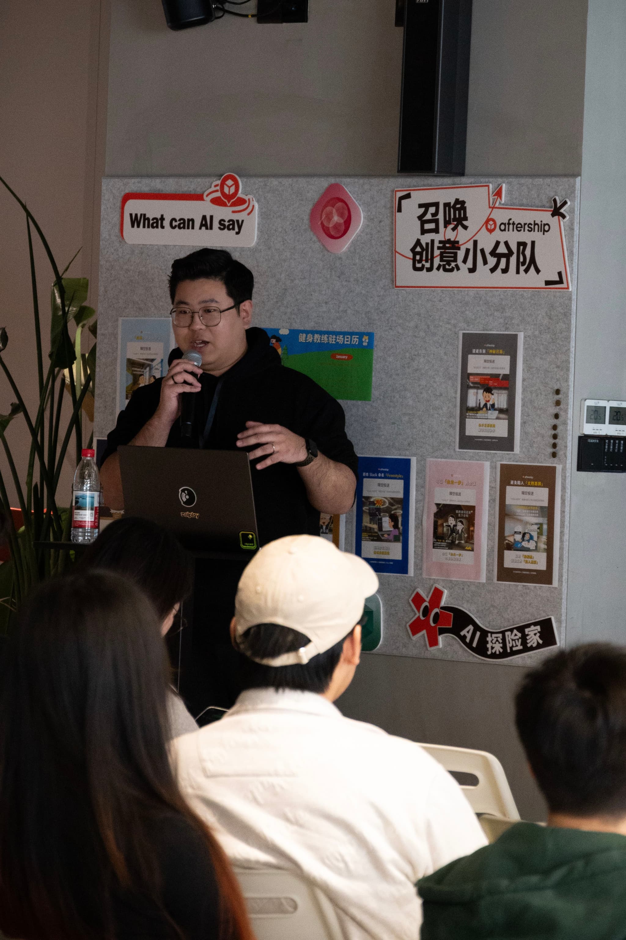 Man speaking into microphone during a small indoor talk while seated attendees watch
