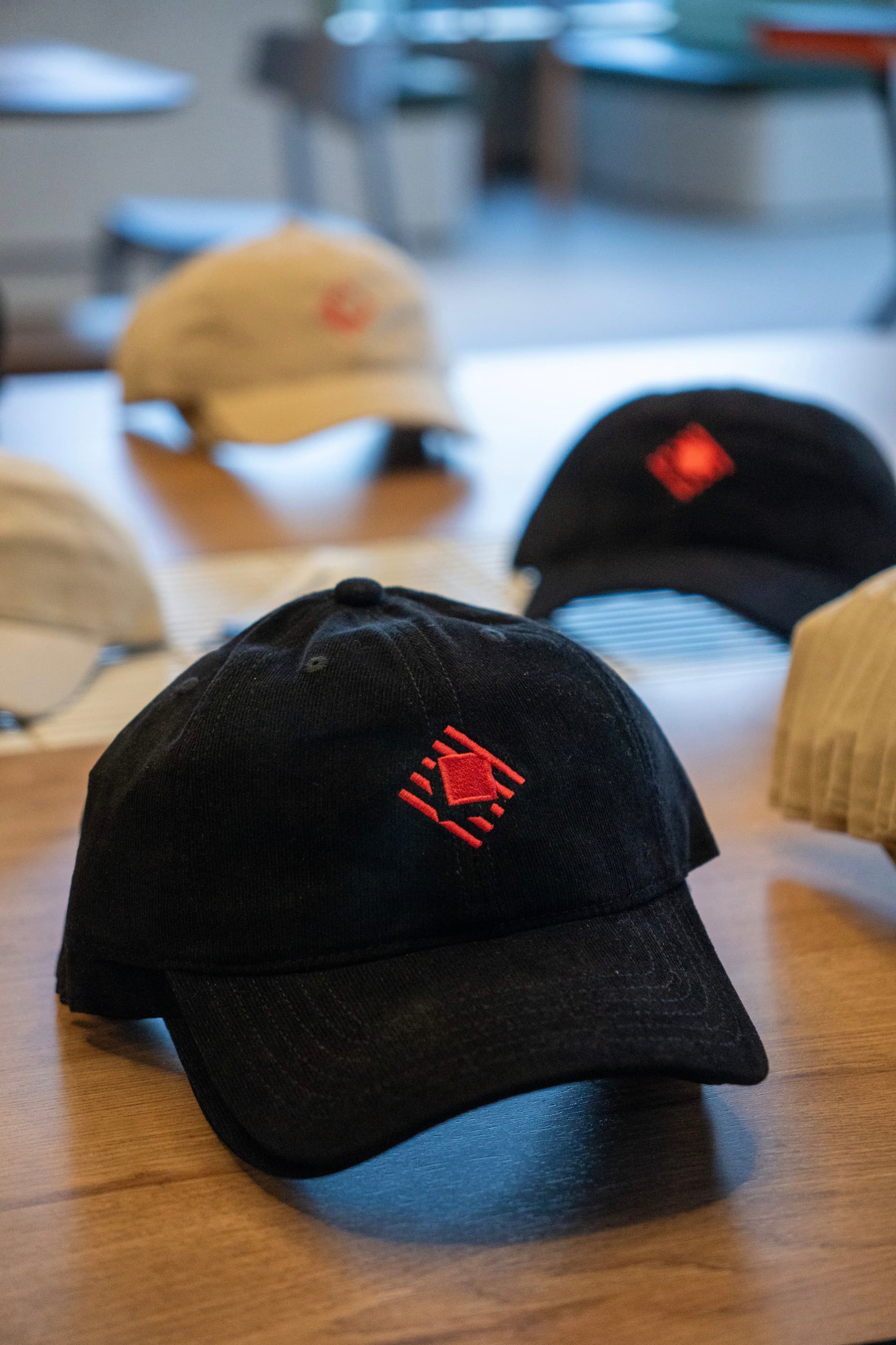 Black baseball cap with red Raycast logo on a table with other caps blurred in the background
