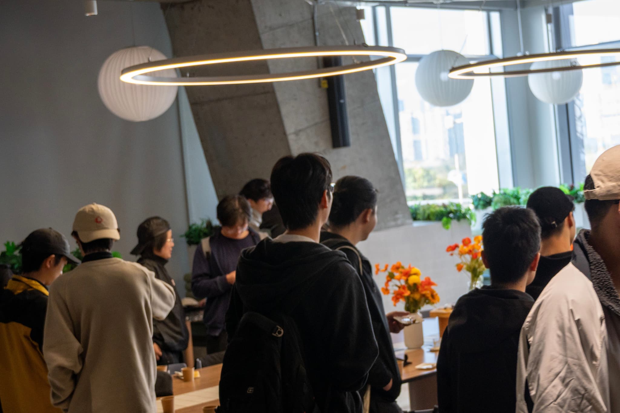 Group of people socializing at an indoor reception with tables of food near large windows