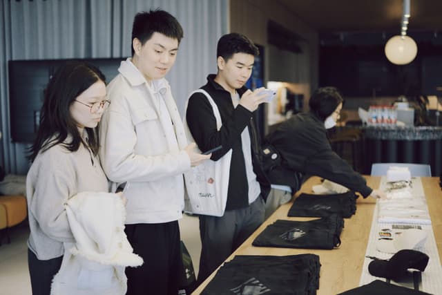Three people in aprons working together behind a cafe counter with trays and equipment