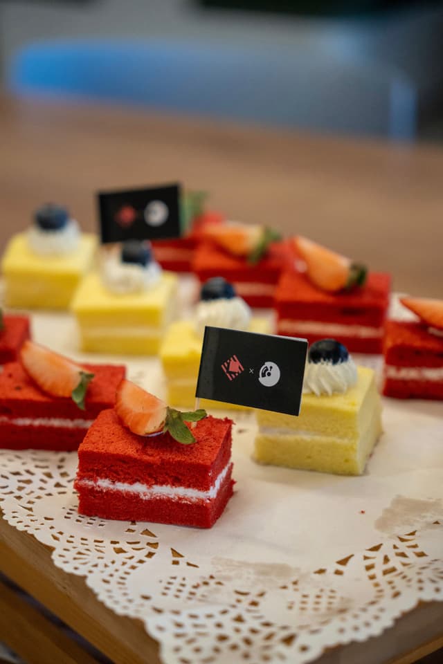 Assorted bite sized layered cakes in red and yellow with small garnish flags arranged on a lace doily plate