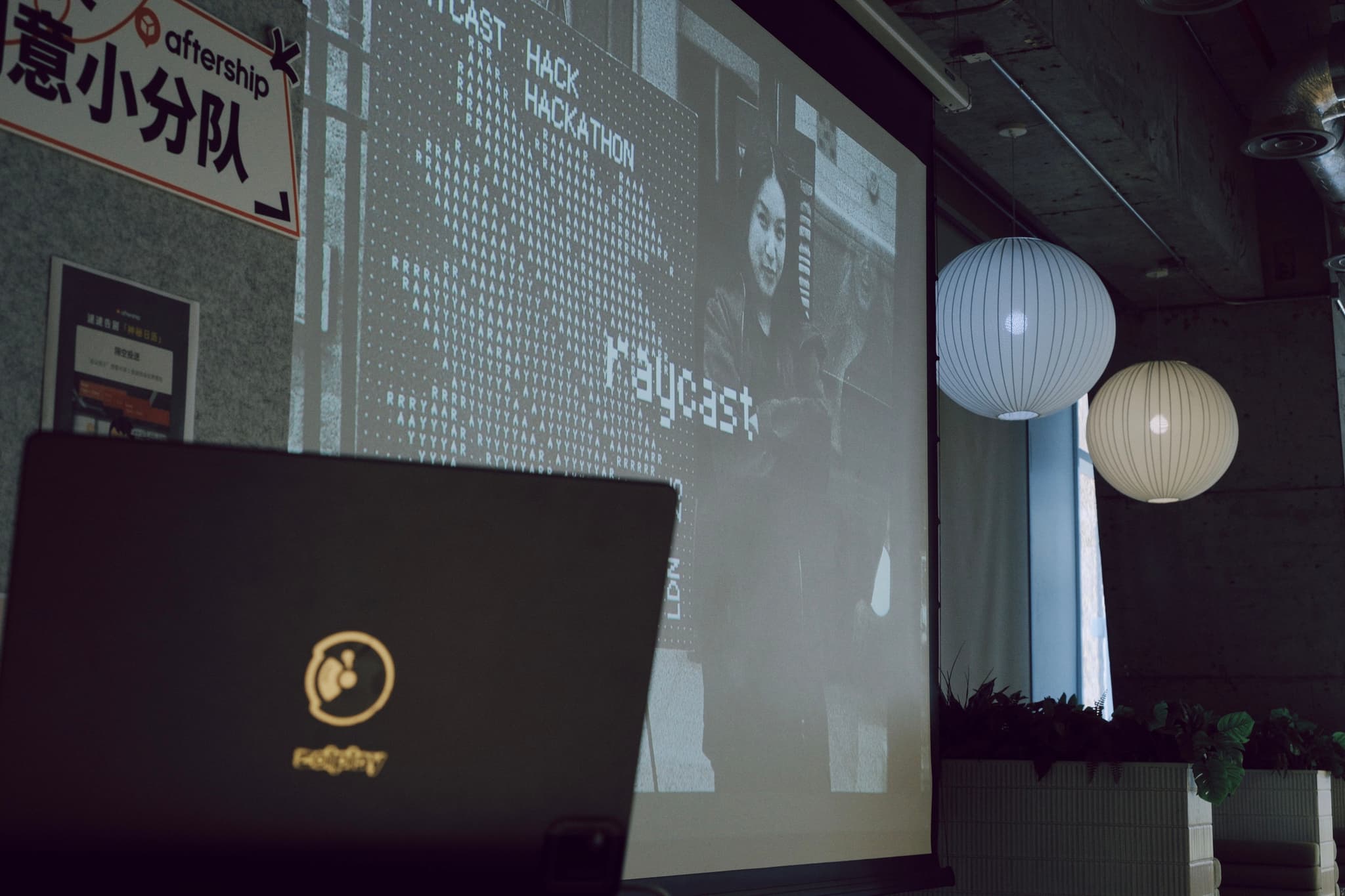 Dim conference room with a projected slide on a large screen and a laptop in the foreground