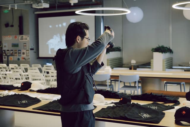 Person arranging equipment in a modern event space with a projected screen, rows of folding chairs, and tables with items laid out