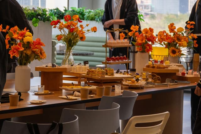 Long dining table set for an event with rustic wooden display stands and floral centerpieces in orange and red tones with chairs in the foreground