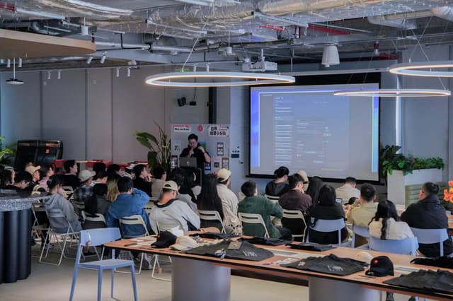 University classroom with students seated at tables watching an instructor present slides on a projector screen