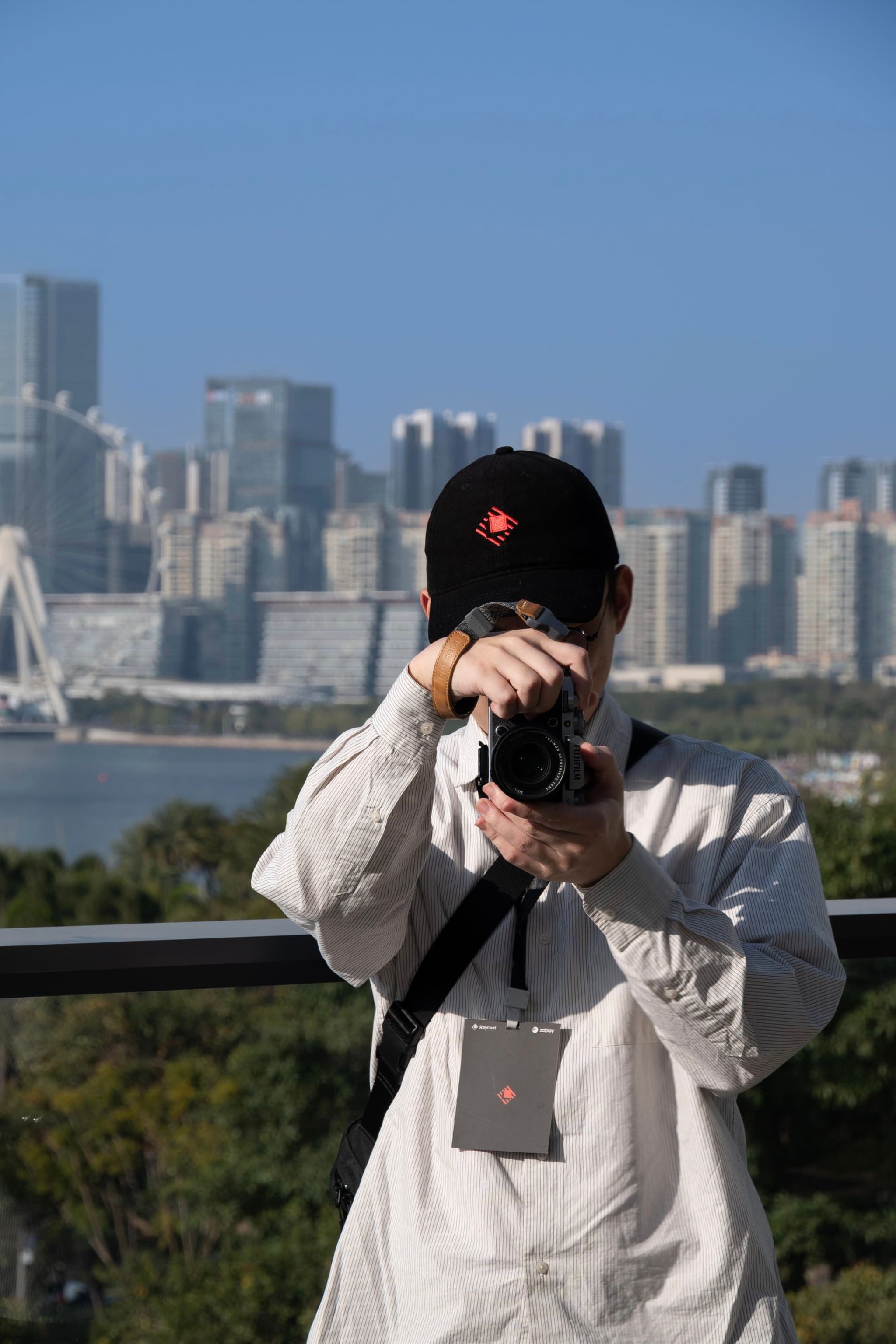 Person wearing a cap photographing a city skyline from an overlook with water and high rise buildings in the background