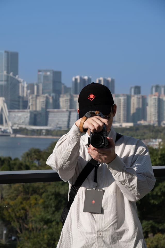 Person wearing a cap photographing a city skyline from an overlook with water and high rise buildings in the background