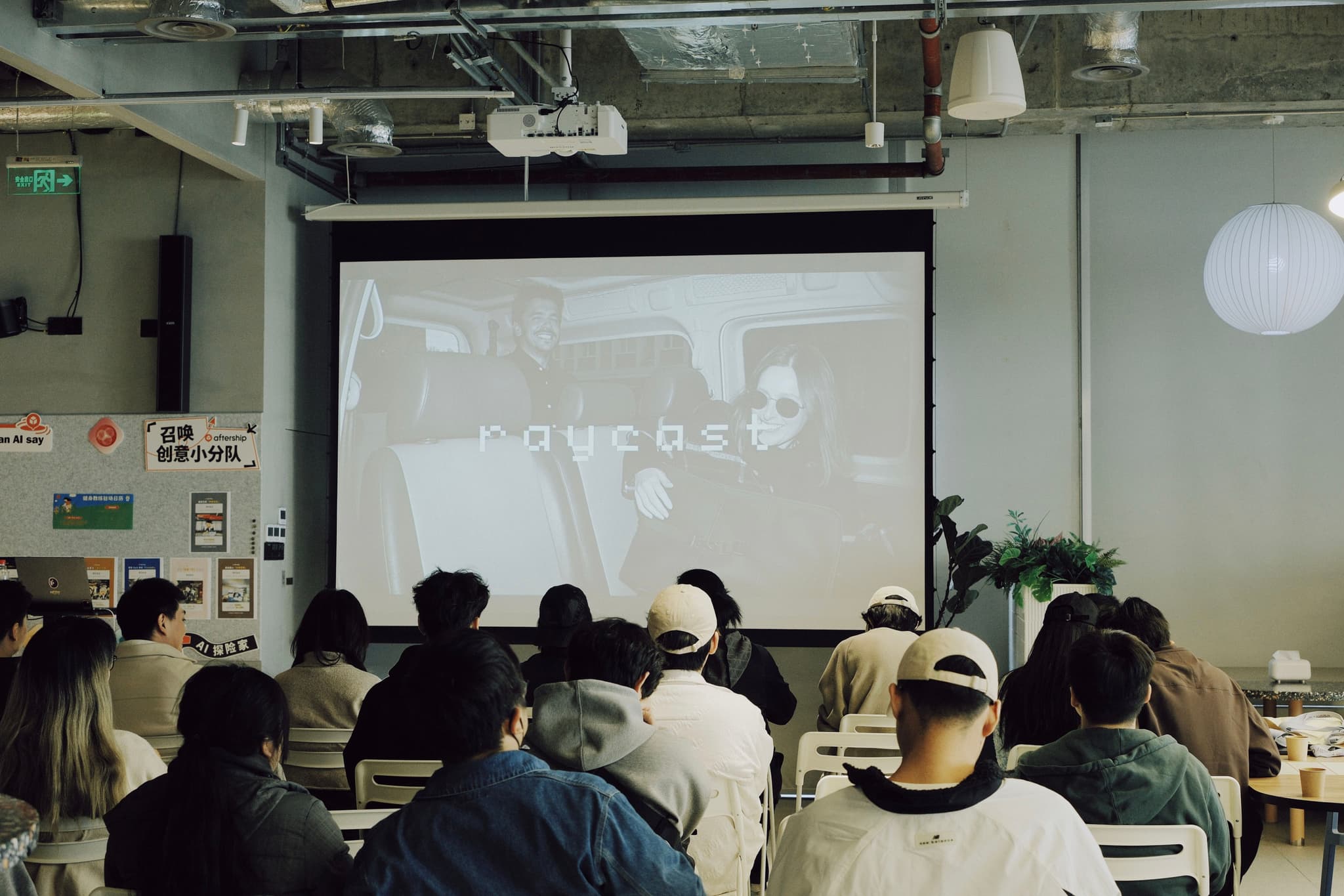 Audience seated in a room watching a presentation projected on a screen at a meetup
