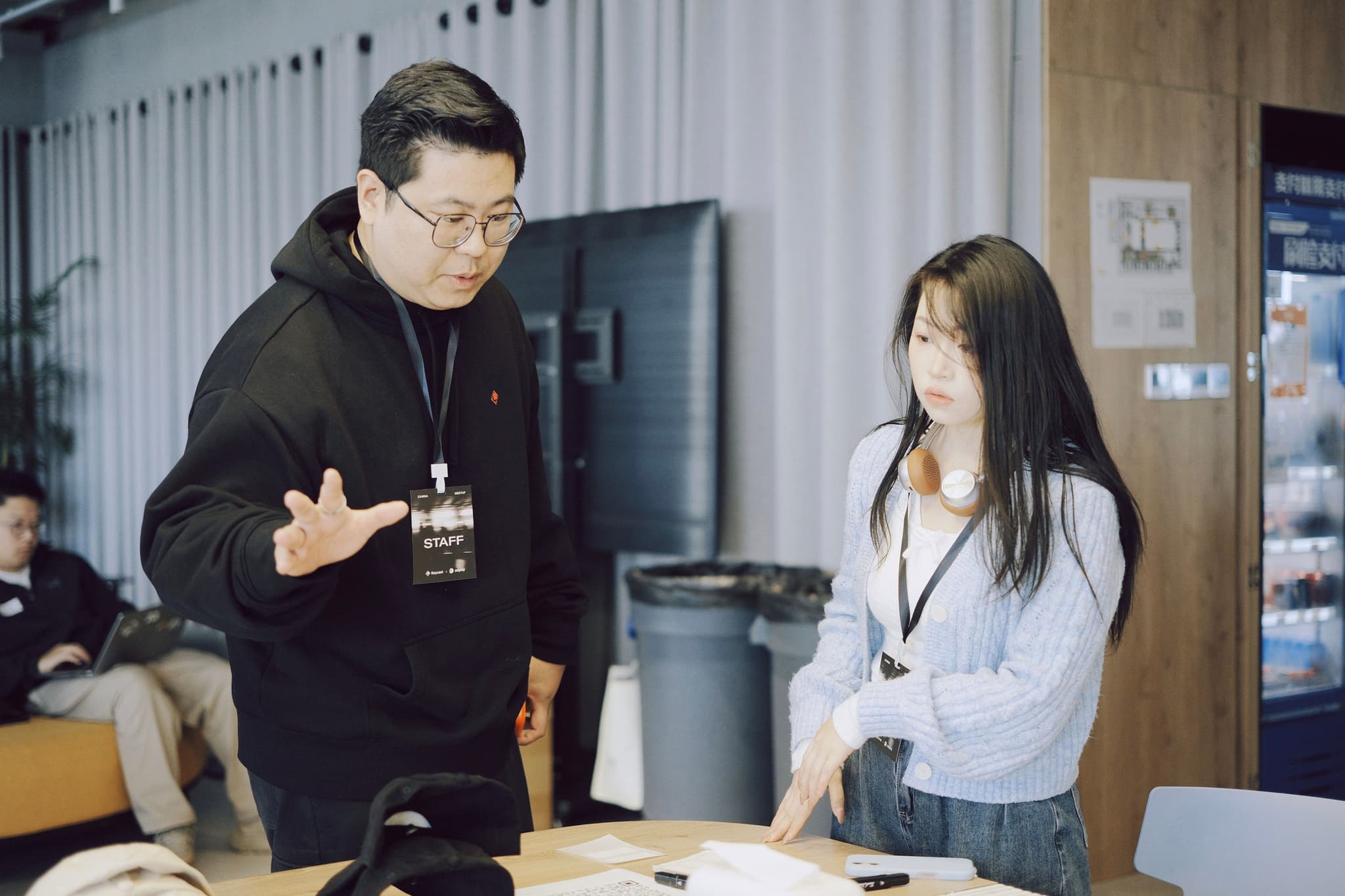 Two coworkers discuss work at a table in an indoor office setting