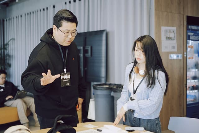 Two coworkers discuss work at a table in an indoor office setting