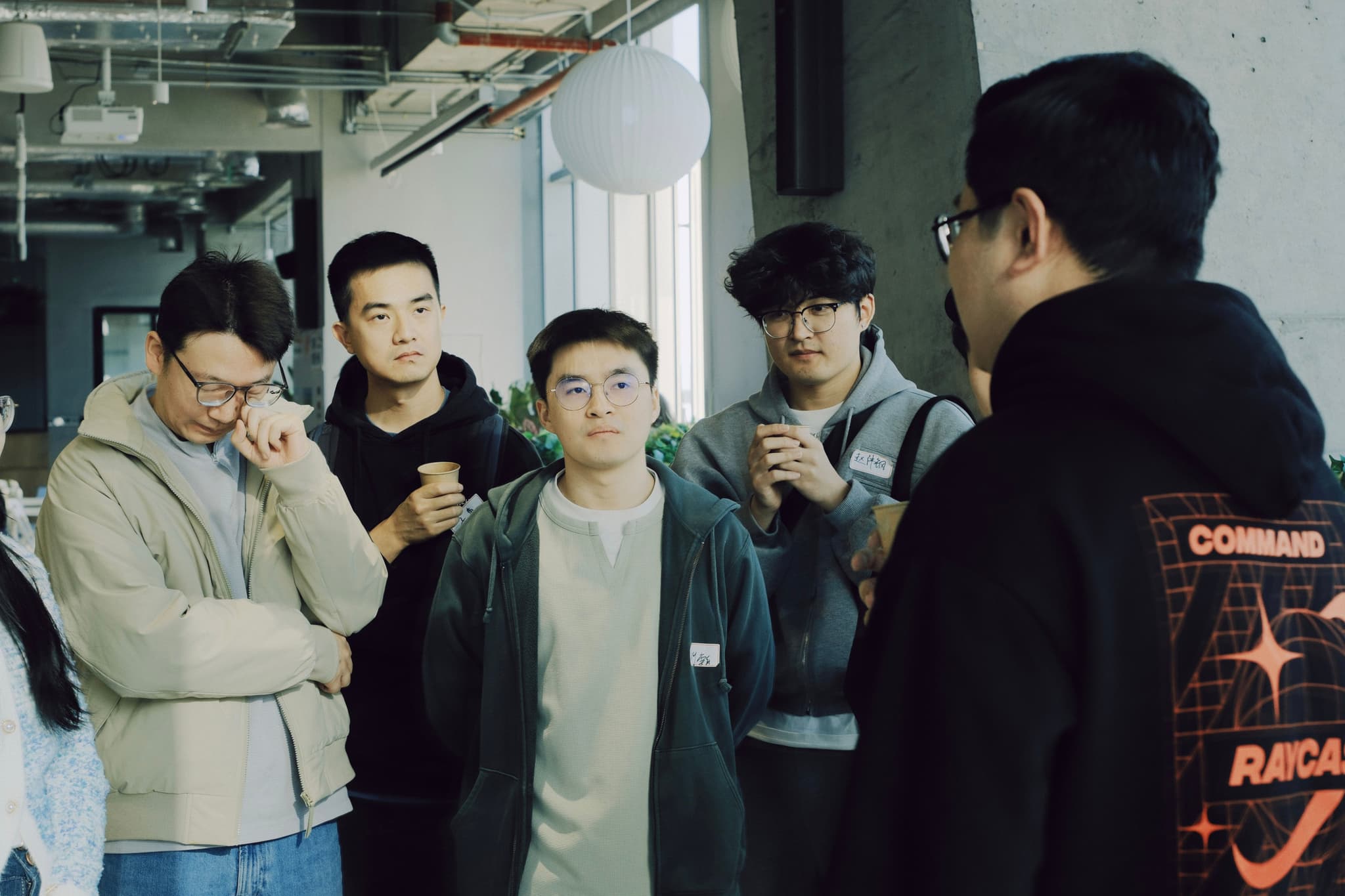 Group of young adults in a workshop space collaborating and reviewing a phone while one person speaks to them