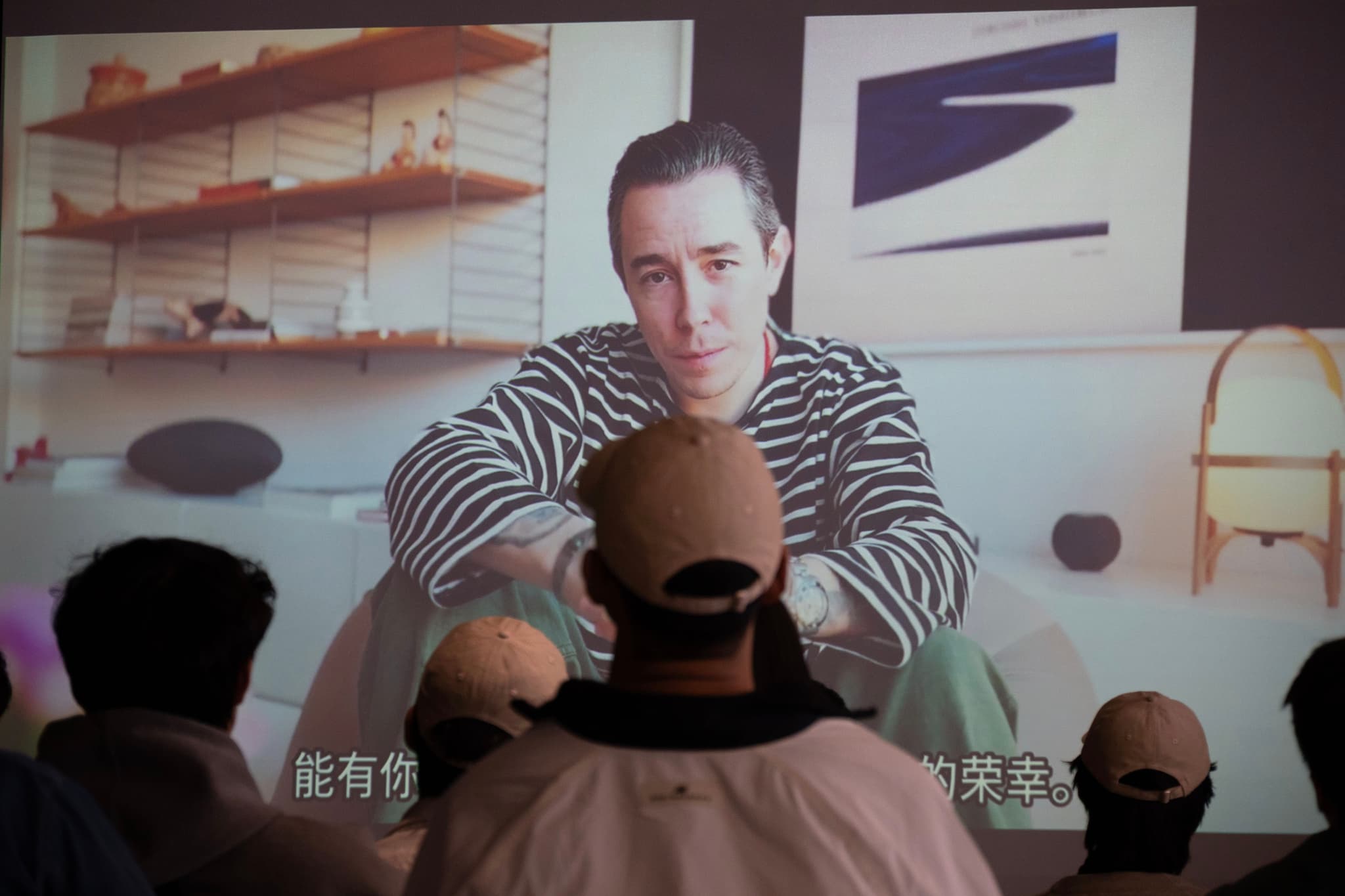 Person in striped shirt sitting facing camera in a softly lit room with another person in the foreground