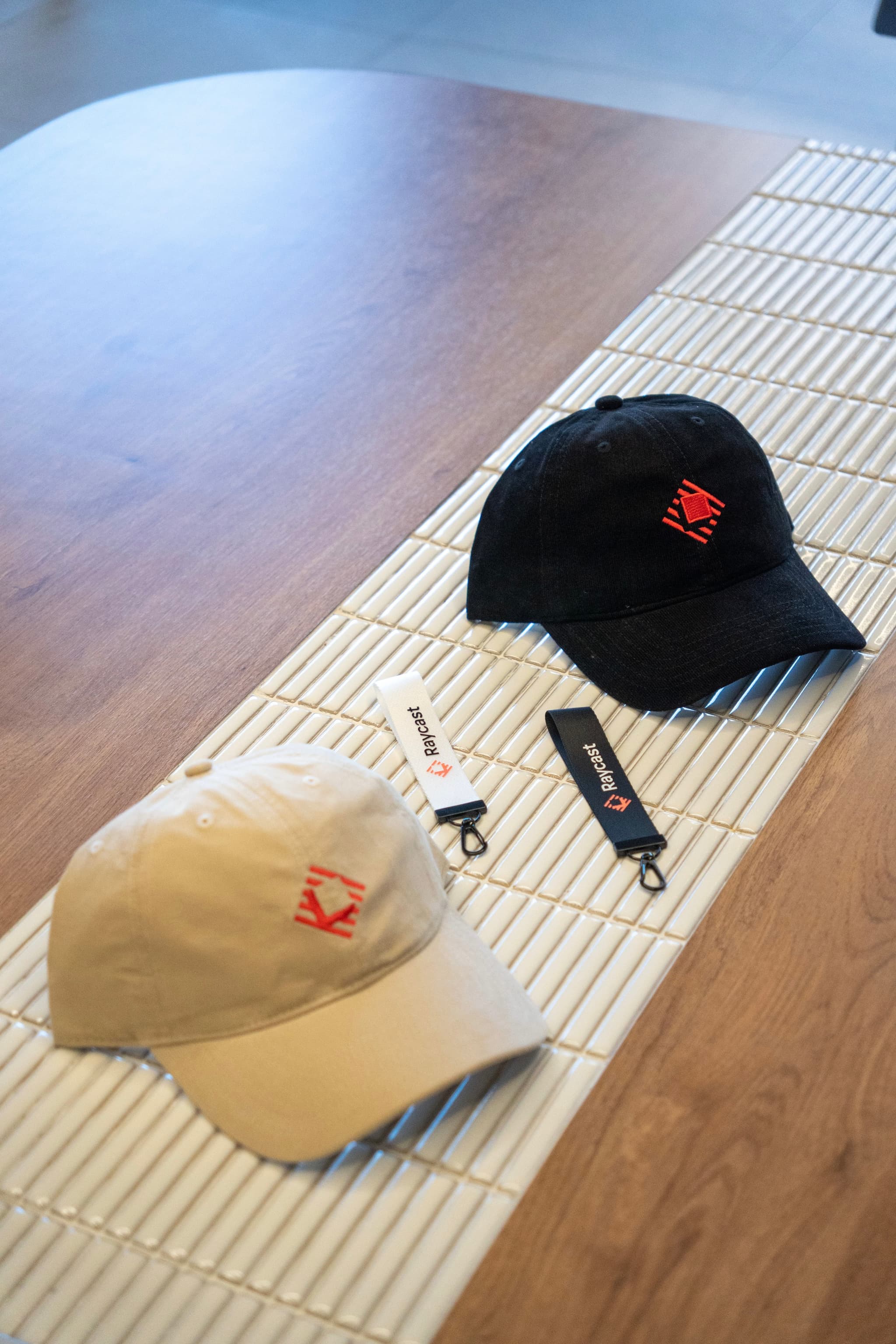 Two baseball caps with small red logos on a striped placemat beside a lanyard on a wooden table