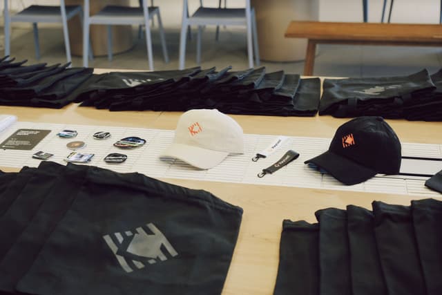 Assorted event merchandise laid out on a table including tote bags, hats, stickers, pens, and lanyards