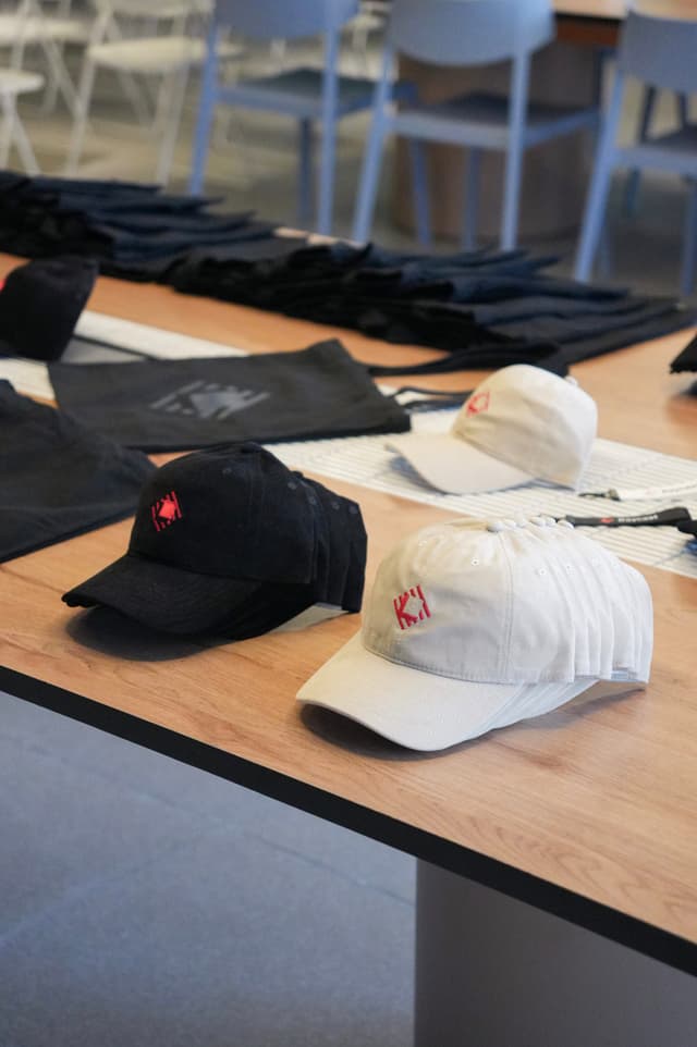 Assorted baseball caps and folded clothing arranged on a wooden table