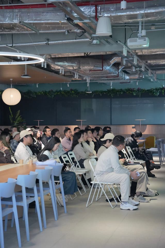 Group of attendees seated on chairs in an industrial style indoor venue with exposed ceiling pipes and lighting