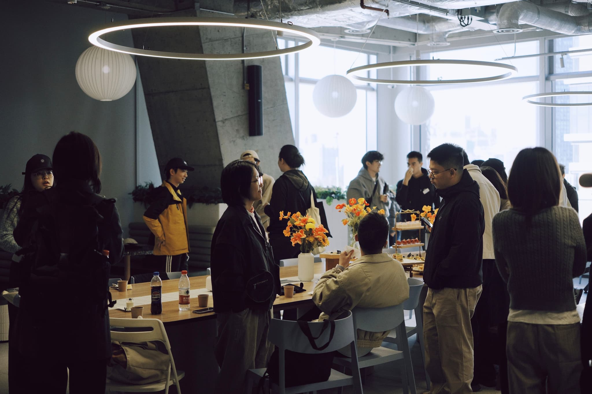 Group of people gathered around a table in a bright office space eating snacks and socializing