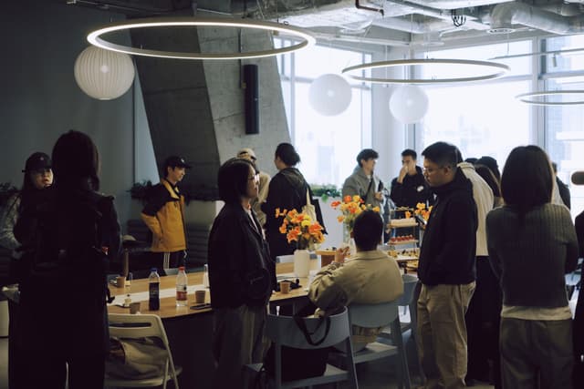 Group of people gathered around a table in a bright office space eating snacks and socializing