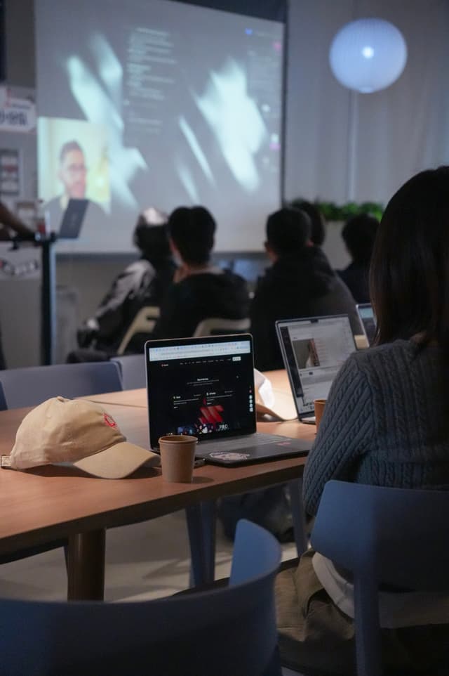 People seated in a classroom watching a projected presentation with laptops open on desks