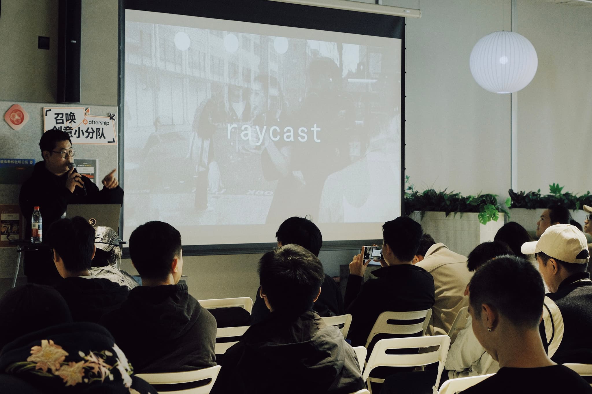 Audience seated in a small meeting room facing a projector screen during a Raycast meetup presentation