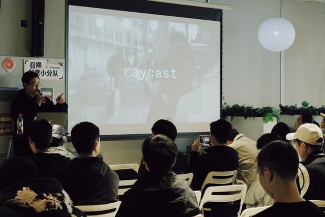 Audience seated in a small meeting room facing a projector screen during a Raycast meetup presentation