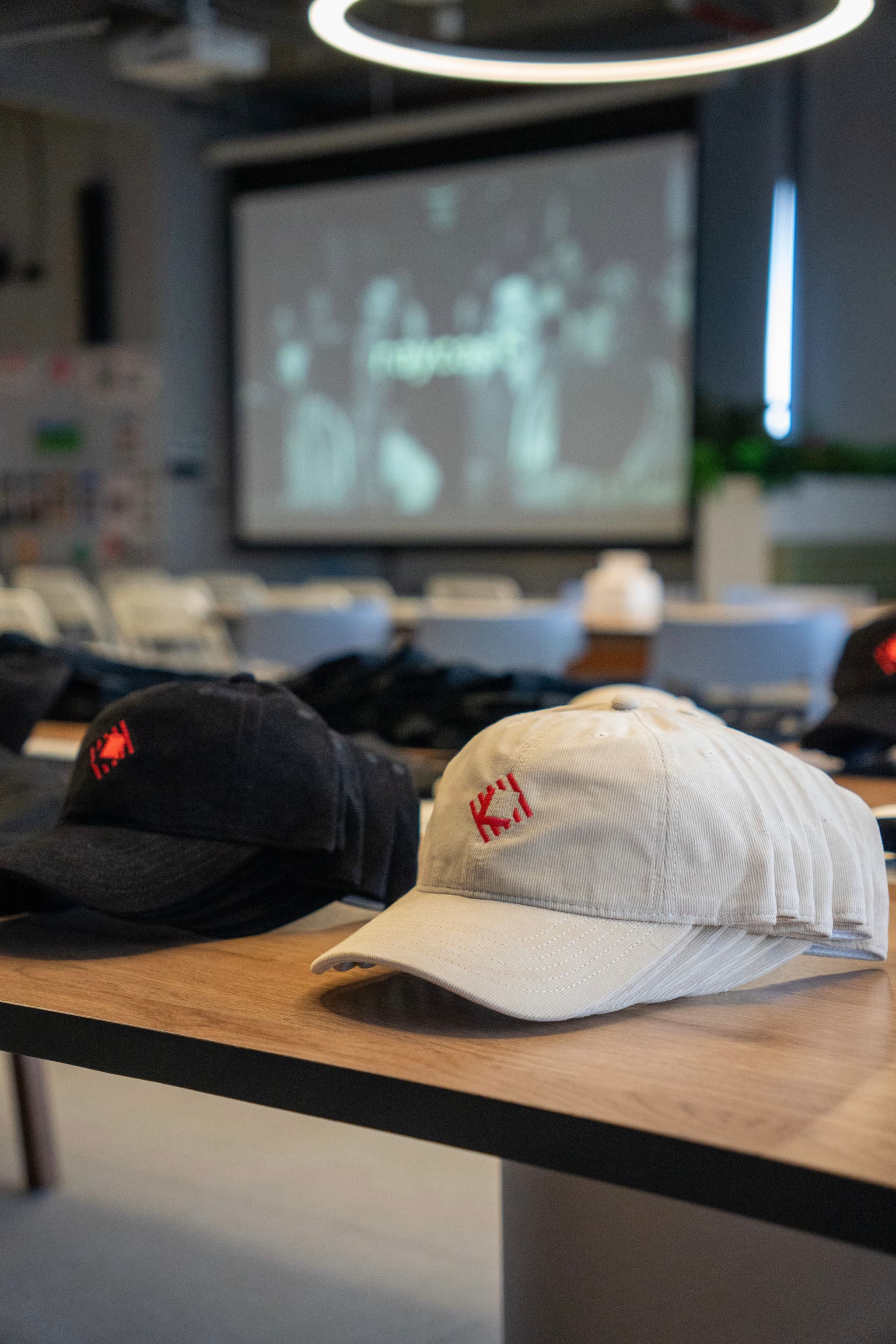 Close up of black and white baseball caps on a wooden table in a classroom with a blurred projector screen in the background