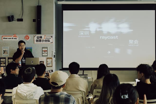 Audience seated in a room watching a projected presentation screen while a presenter stands to the side