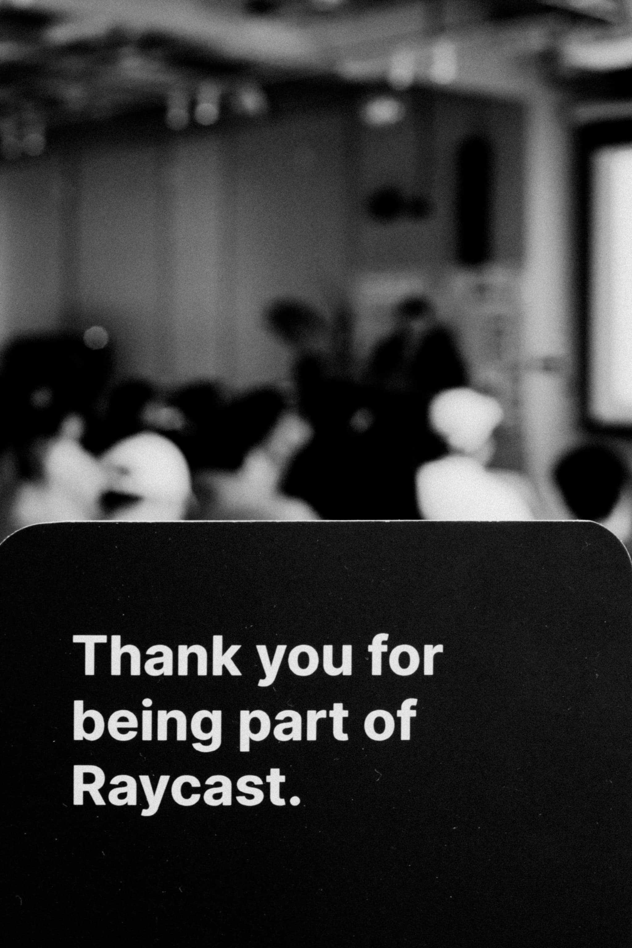 Blurred audience seated at a meetup with a sign reading Thank you for being part of Raycast