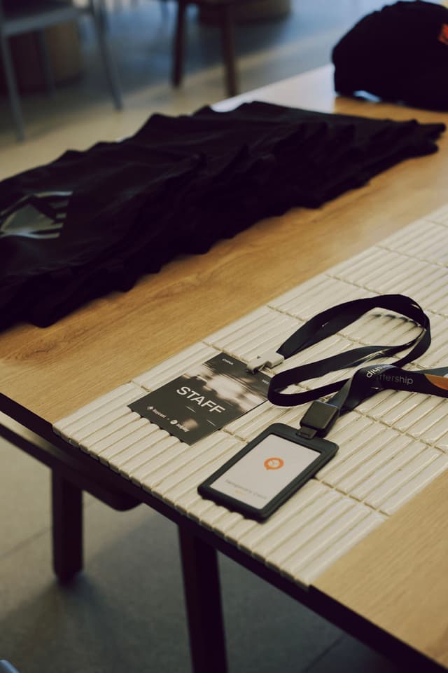 Wooden table with lanyard, name badge, and event flyers laid out in a meeting space