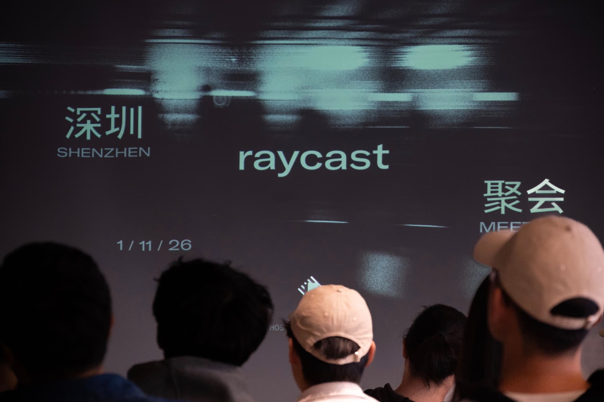 Audience silhouettes facing a screen showing Raycast branding and Chinese text at a meetup event