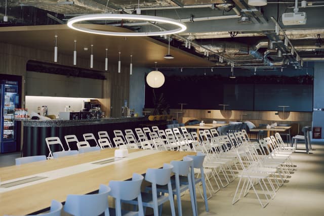 Modern event space with long tables and rows of white folding chairs under circular ceiling lights