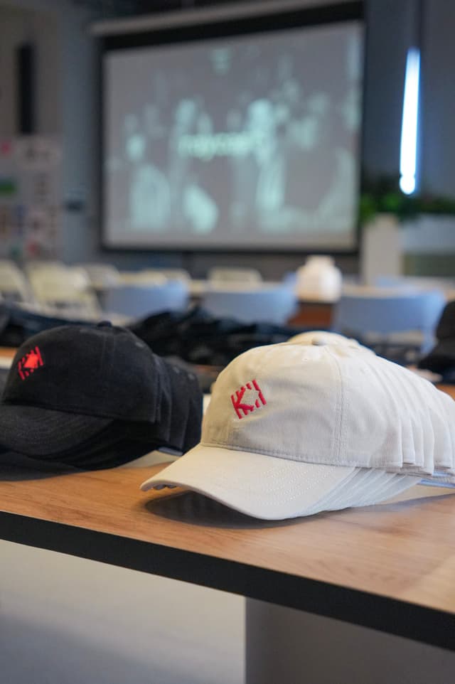 Two baseball caps on a wooden table with a blurred presentation screen in the background