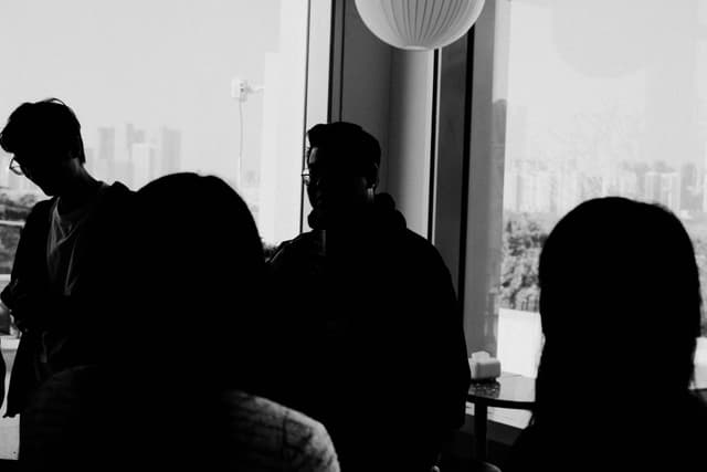 Silhouetted people conversing near large windows with a city skyline outside