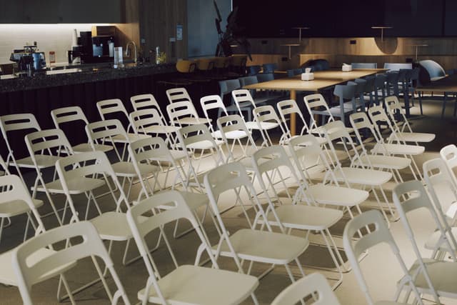 Rows of white folding chairs arranged in an indoor auditorium with a stage in the background