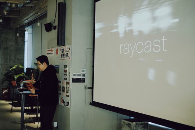 Presenter stands beside a large projected screen in a conference room