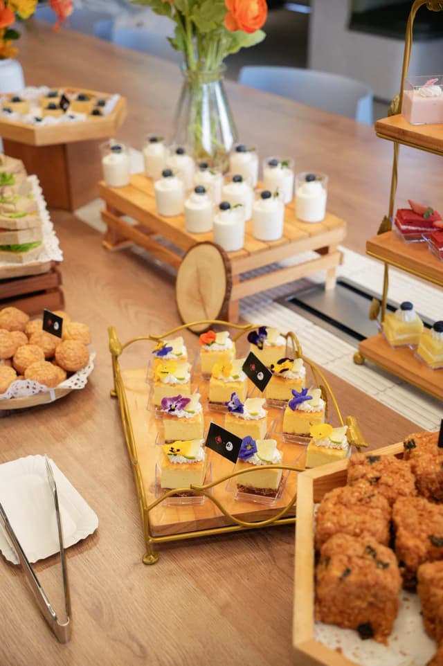 Buffet table with assorted pastries sandwiches fried bites and small dessert cups on wooden and tiered stands