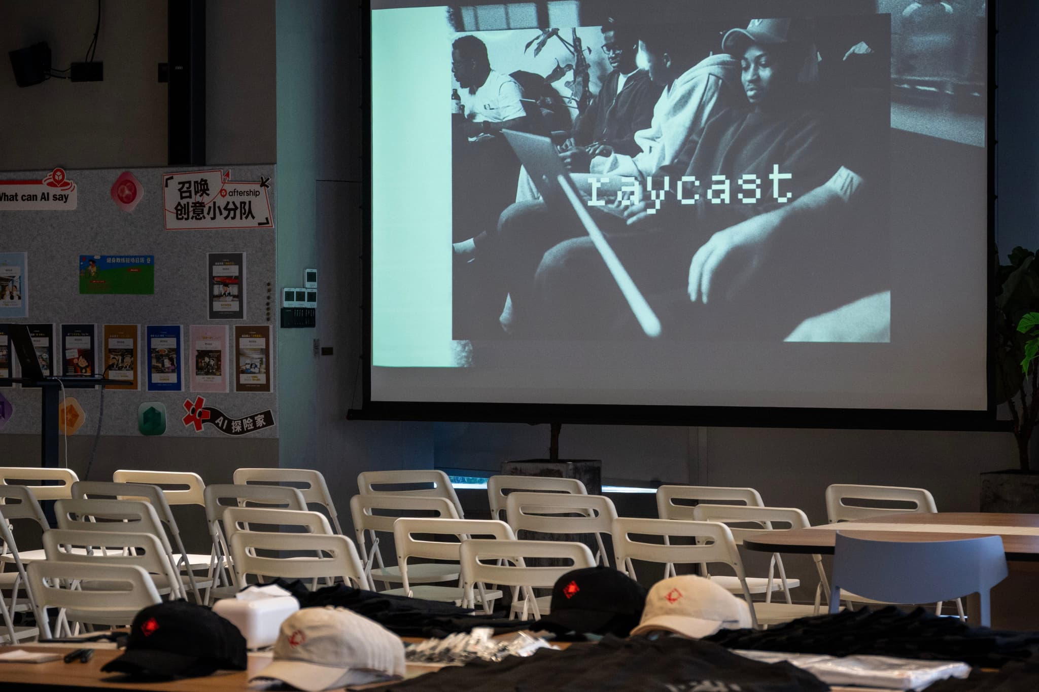 Empty conference room with rows of chairs facing a large screen showing a Raycast slide