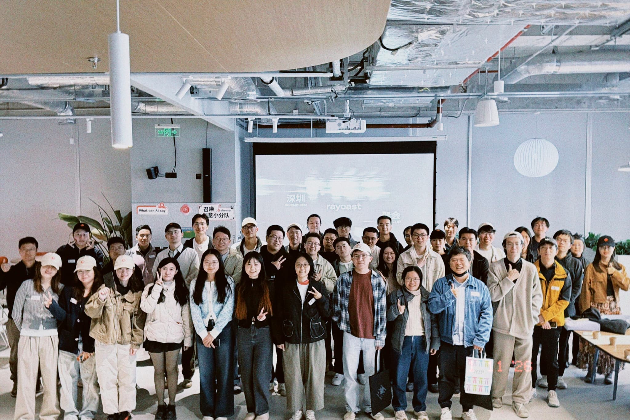 A large group of people standing together in a bright, modern office space for the Shenzhen Raycast Meet-up, facing the camera.