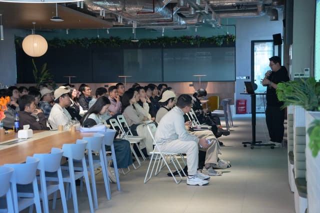 Large group seated in a modern conference room watching a presenter near a screen
