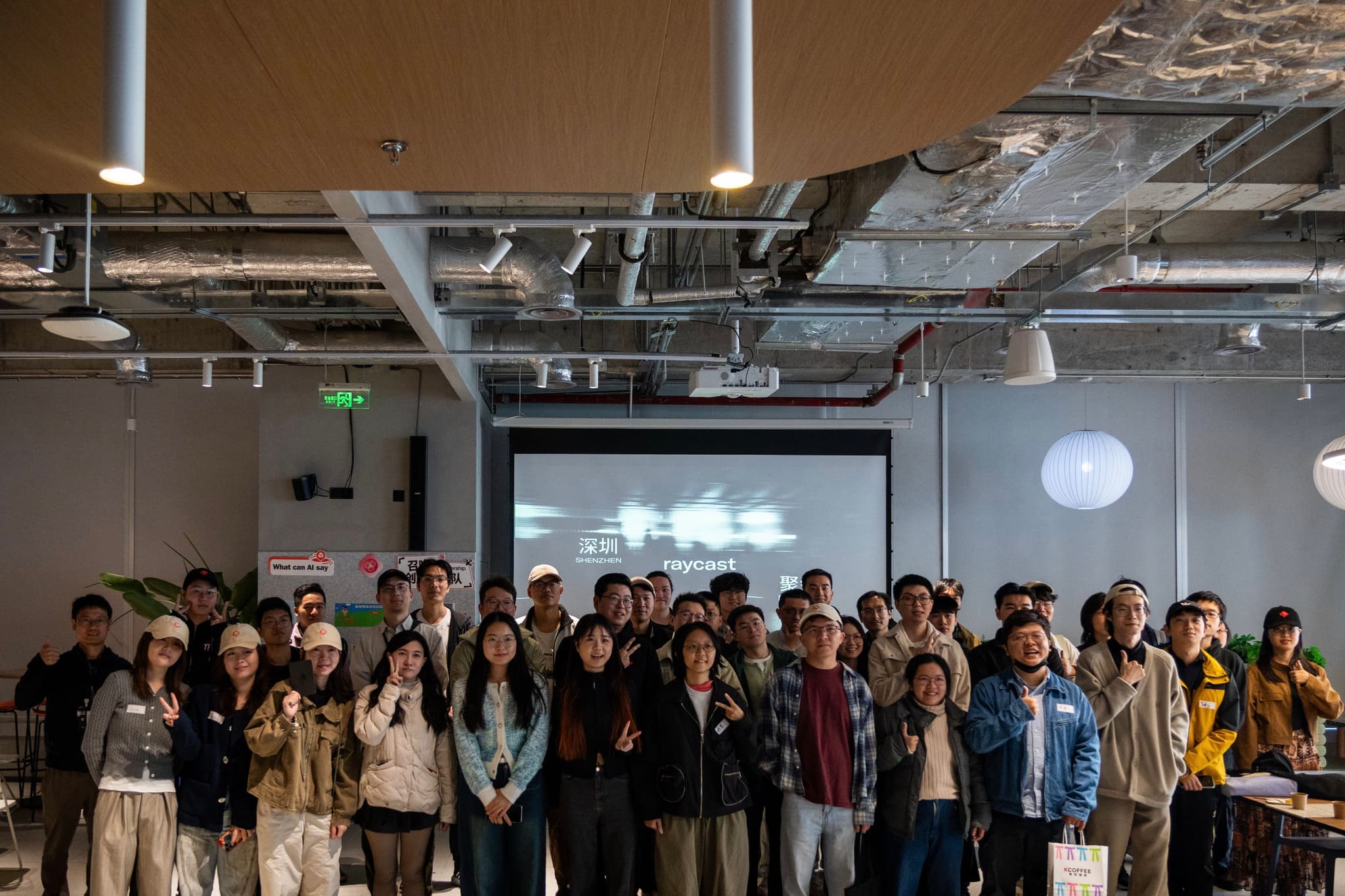 Large group of people standing together indoors in a modern event space with a projected screen in the background