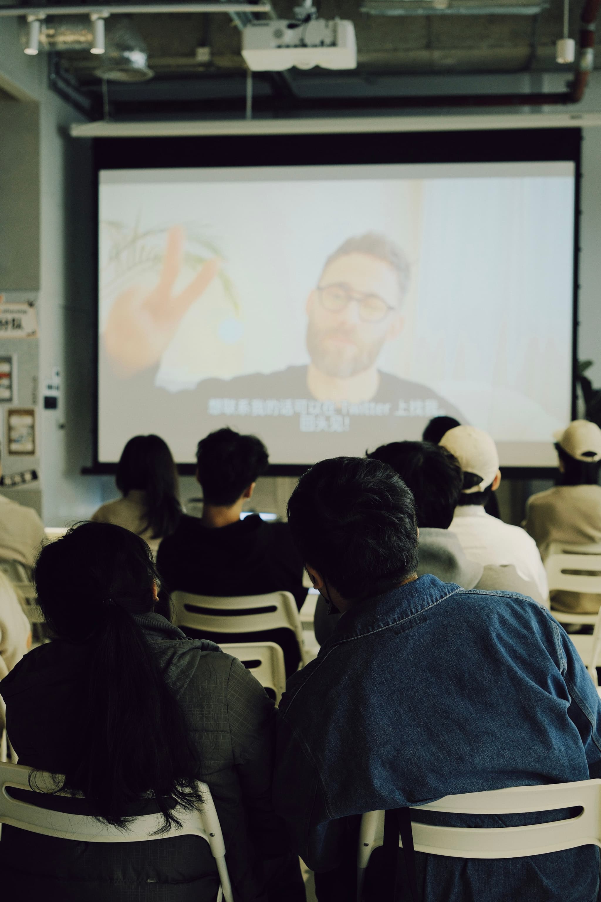 Audience seated on folding chairs watching a projected video in an industrial room