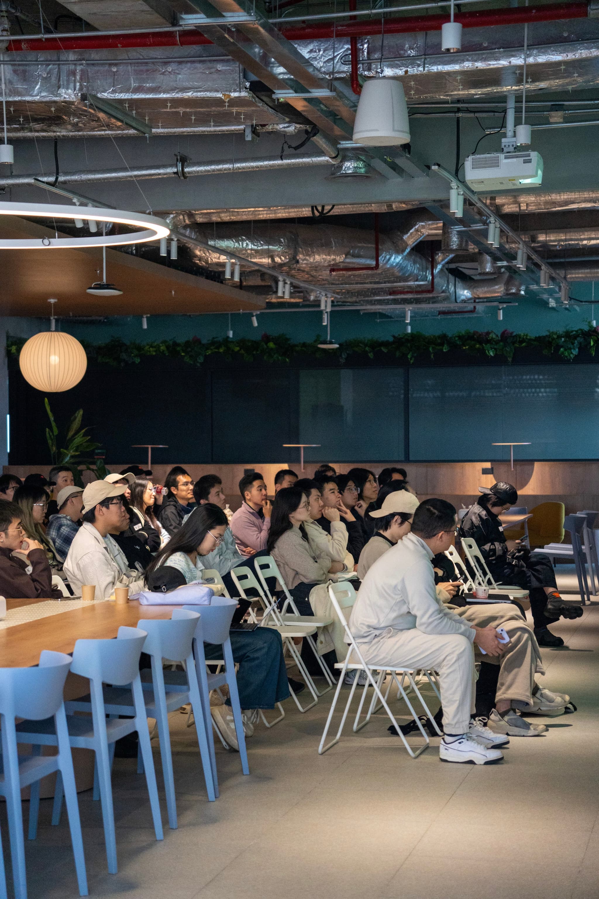 Seated audience listening in an industrial style event space with exposed ceiling, bar seating on the left, and a presenter area in front