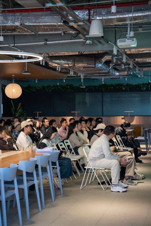 Seated audience listening in an industrial style event space with exposed ceiling, bar seating on the left, and a presenter area in front