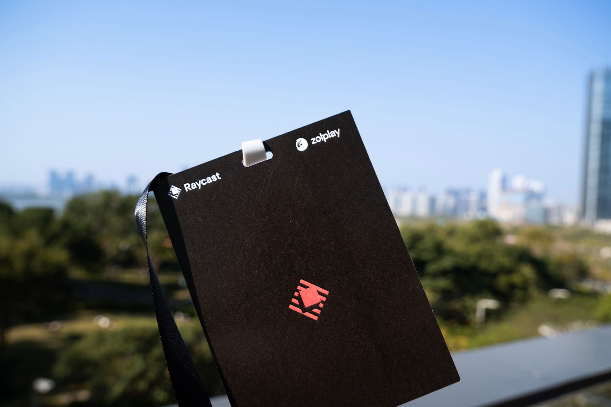 Close up of a black badge with a red emblem held outdoors with a blurred city skyline and trees in the background