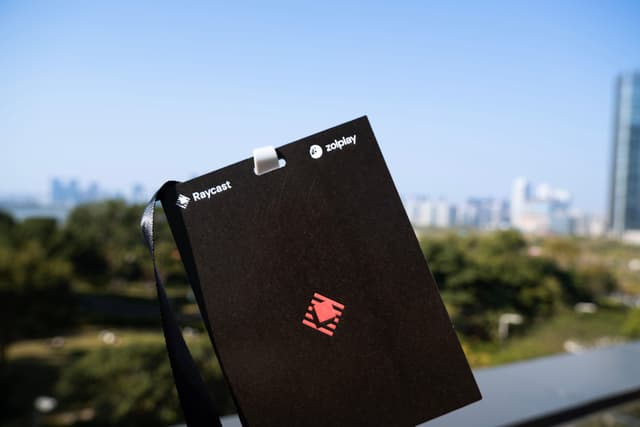 Close up of a black badge with a red emblem held outdoors with a blurred city skyline and trees in the background