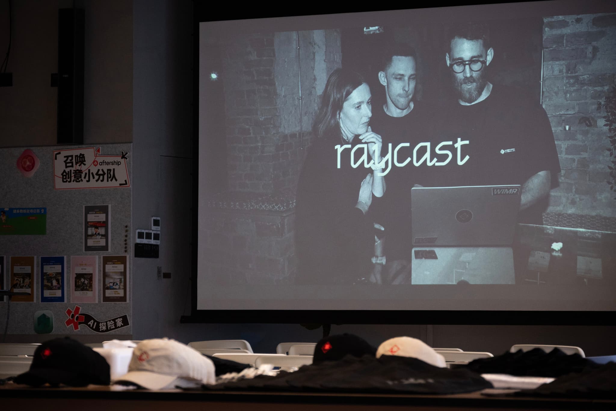 Person presenting raycast software on a large projected screen in a dim room with seats and papers in the foreground