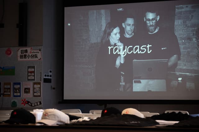 Person presenting raycast software on a large projected screen in a dim room with seats and papers in the foreground