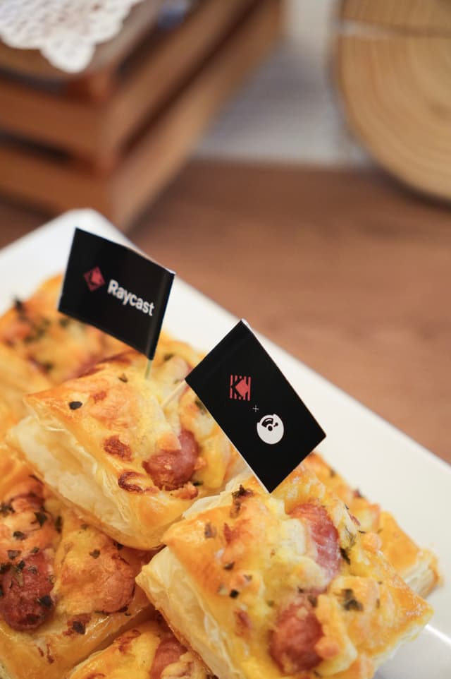 Closeup of cheesy bacon topped pastry squares on a white plate with small black flags in a warm rustic setting